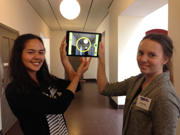 Jennie and Cathrine holding an iPad with CamQuest open and camera showing a round lamp inside the app's circle.